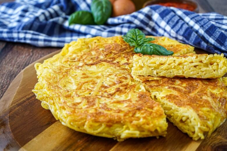Goldbraune Frittata di Pasta in der Pfanne, außen knusprig, innen saftig, mit Kräutern bestreut – klassisches neapolitanisches Resterezept.